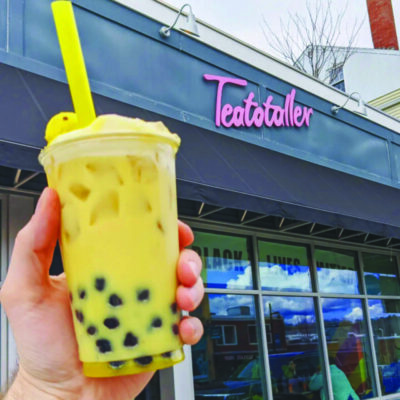 hand holding boba tea in front of outside of shopfront