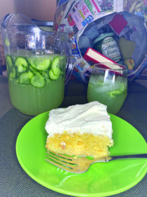 pitcher and glass filled with cucumber margarita beside plate of cake