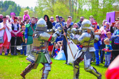 men in armor fighting in front of audience at Renaissance faire.