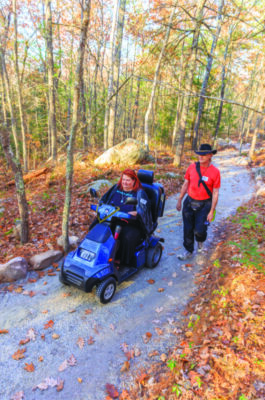 woman in motorized scooter and man on hiking trail in autumn
