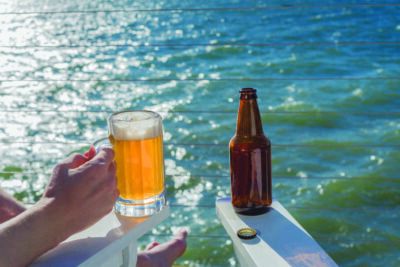Mans hand holding freshly poured beer in mug on seaside deck