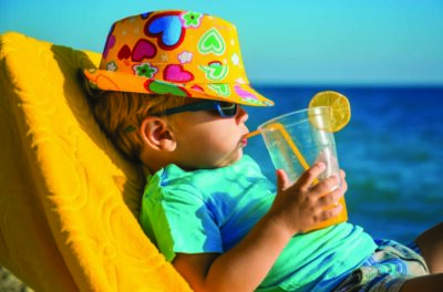 Boy kid in armchair with juice glass on beach against sea