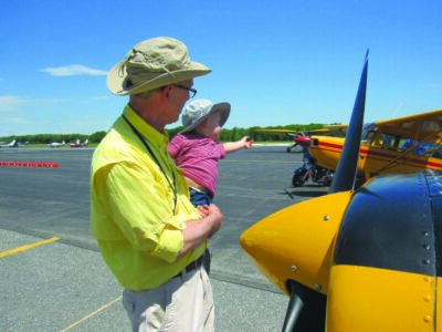 man holding baby, looking at small airplane