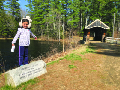 young girl standing on historic stone in front of covered bridge