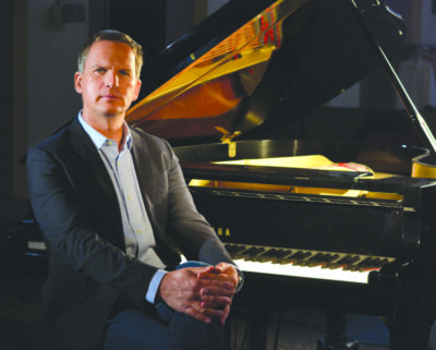 middle aged man wearing suit, sitting in front of piano