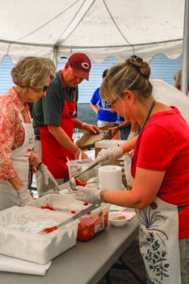volunteers preparing strawberries with ice cream at tables for strawberry festival