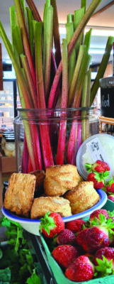 rhubarb stalks in jar, with bowl of biscuits and box of strawberries on counter