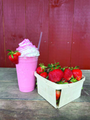 strawberry frappe with whipped cream topping, beside container of strawberries on table outside