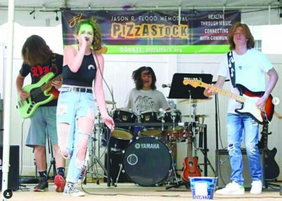4 band members performing on outdoor stage, sunny day