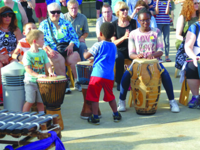 children playing large drums at outdoor event, adult audience watching