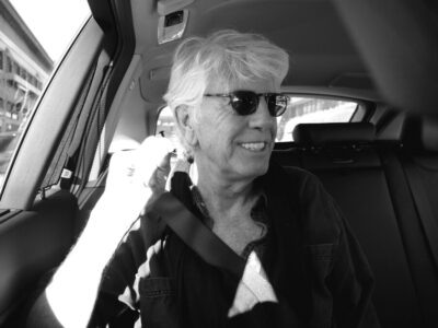 headshot of Graham Nash, elder man wearing sunglasses, sitting in car
