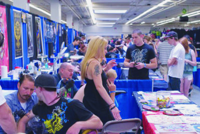 people at booths and behind tables featuring artwork at tattoo expo