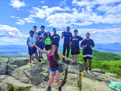 group of young people posing on rocks at top of mountain after hike