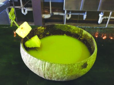 coconut bowl filled with kava drink and 2 pineapple pieces on cocktail skewer