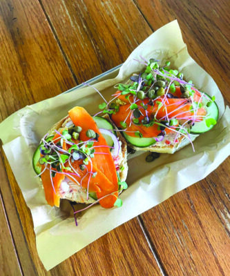 2 bagel halves topped with lox, sliced carrots, and sprouts in takeout container on wooden surface