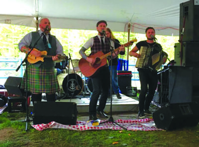 3 men playing instruments in outdoor tent venue, dressed in plaid