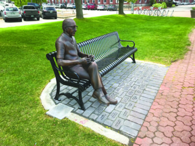 park bench with statue of man sitting, bricks with names carved on them beneath bench