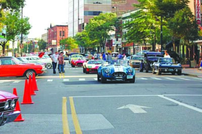 classic cars driving in line down city street