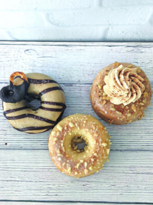 3 donuts with various toppings and glazes, on wooden surface