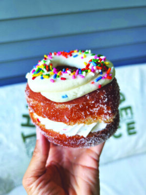 hand holding fancy donut with cream inside and frosting and rainbow sprinkles on top