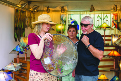 a craftsperson displays a piece of glass artwork to a man and a woman