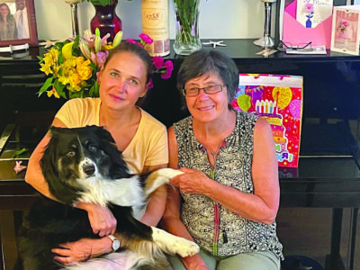 two women, one middle aged, one older, sitting on a piano bench, holding large dog