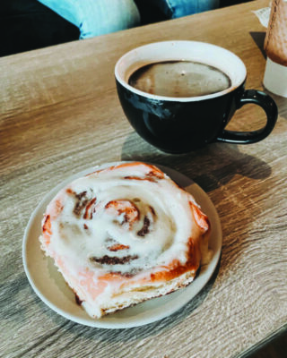 cinnamon bun with frosting beside cup of coffee on table