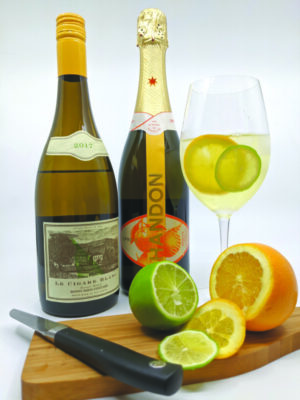 2 bottles of wine beside cutting board containing sliced orange and lim and wine glass