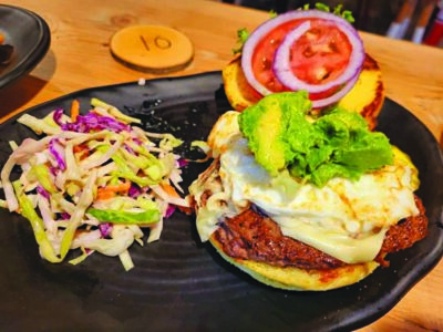 burger with cheese and avocado, tomoto and onion, on open bun, with bowl of coleslaw, on table