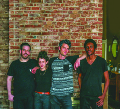 4 band members posing in front of brick wall