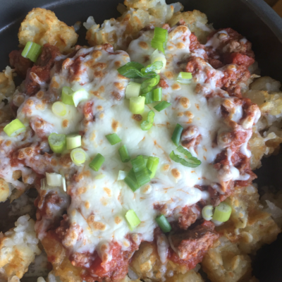 close up of tater tot waffle topped by sour cream, ground beef, and chopped scallions