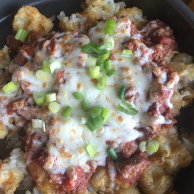 close up of tater tot waffle topped by sour cream, ground beef, and chopped scalllions