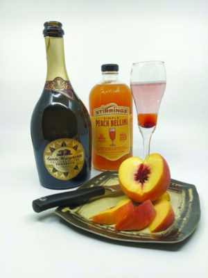 bottle of wine, bottle of peach puree, sitting beside wine glass and plate with cut up peach