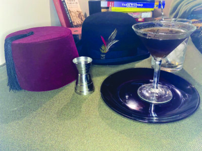 cocktail glass on table beside a bowler hat and a fez