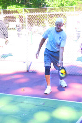 a white haired and bearded man serves the ball on a pickleball court