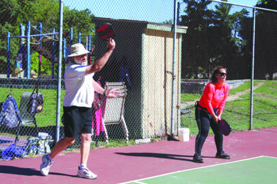 a man and a woman on a pickleball court, man serving the ball