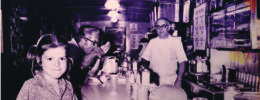 historic photo of diner counter, young girl looking at camera, man eating, man behind the counter