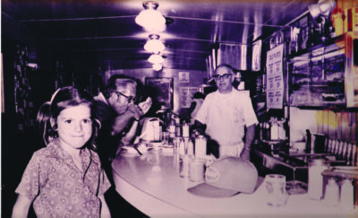 historic photo of diner counter, young girl looking at camera, man eating, man behind the counter