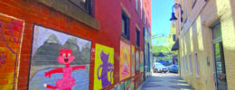 pedestrian alley between brick buildings, painted murals of cats on the side of one building