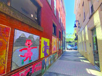pedestrian alley between brick buildings, painted murals of cats on the side of one building