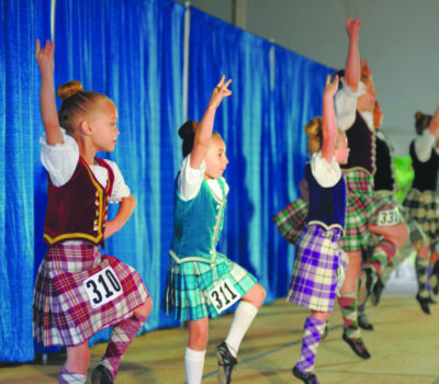 girls dressed in kilts and vests dancing on stage in traditional Scottish dance competition