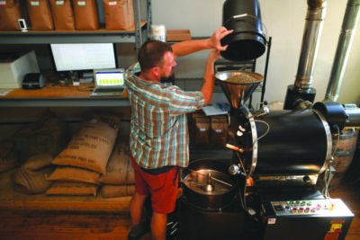 man pouring coffee beans into large machine