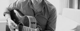Black and white photo of Chris Trapper, a very rock and roll looking younger man playing an acoustic guitar.