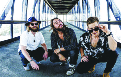 3 male band members crouching on walkway with glass walls, promotional photo