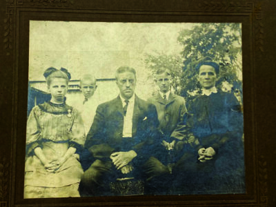 vintage photograph of 5 member family, serious expressions, a man, a woman, 2 boys, a girl