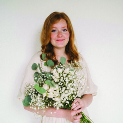 young woman on white background, holding bouquet of white flowers, smiling