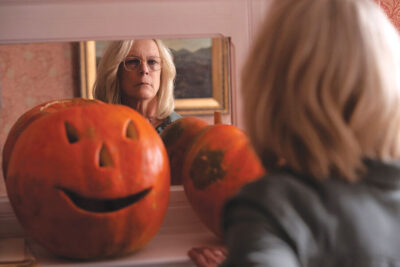 Jamie Lee Curtis killing it in Halloween Ends. Standing in front of a mirror with amazing shoulder length silver hair, and surrounded by creepy jack-o-lanterns