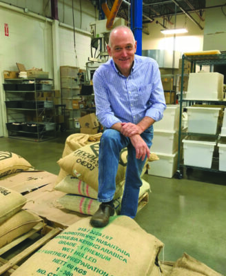 man standing with one foot on canvas bags of coffee in warehouse