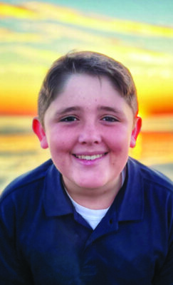 headshot of smiling boy in front of setting sun