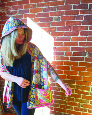 woman standing in font of brick wall modeling a colorful hooded jacket with front pocket
